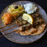 3 spiezen van buikspek, geserveerd met friet, tzatziki, koolsalade en een pita